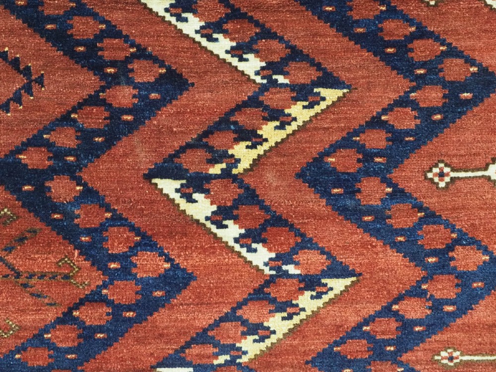 A rectangular hand-knotted wool chuval face featuring red and navy blue geometric chevron ikat patterns within decorative borders. View IX