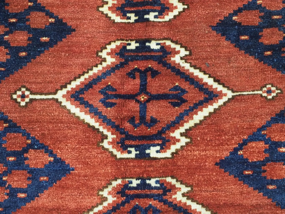 A rectangular hand-knotted wool chuval face featuring red and navy blue geometric chevron ikat patterns within decorative borders. View X