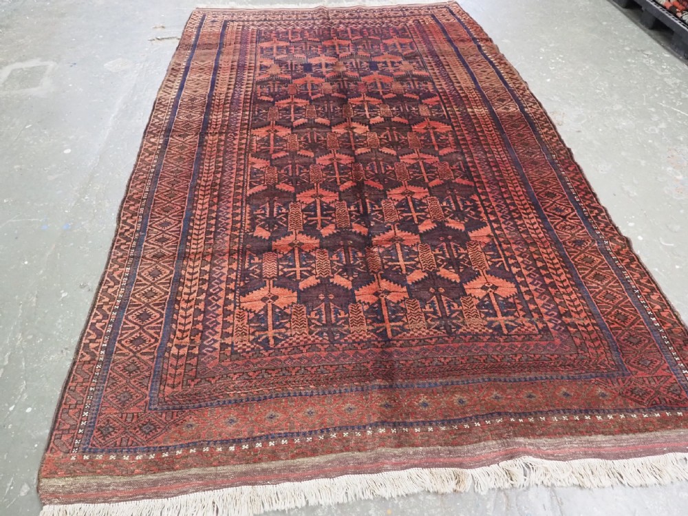 An antique Afghan Baluch hand-knotted wool rug featuring dark red, indigo, and terracotta geometric repeating motifs and ornate multi-layered borders. View II