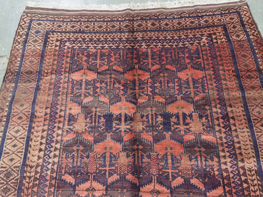 An antique Afghan Baluch hand-knotted wool rug featuring dark red, indigo, and terracotta geometric repeating motifs and ornate multi-layered borders. View III