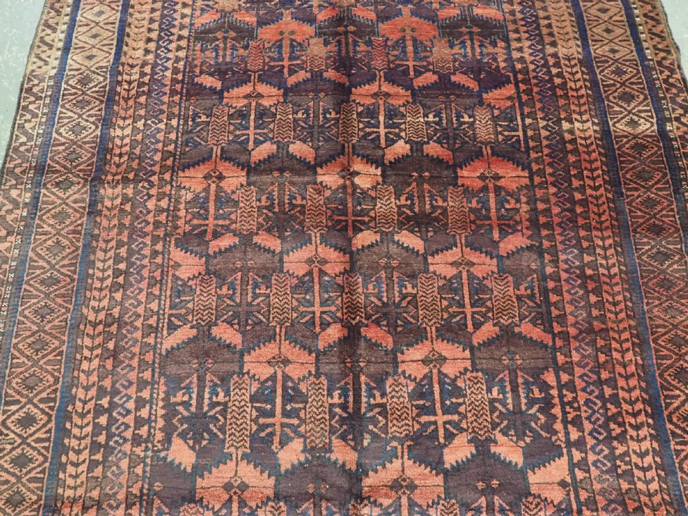 An antique Afghan Baluch hand-knotted wool rug featuring dark red, indigo, and terracotta geometric repeating motifs and ornate multi-layered borders. View IV