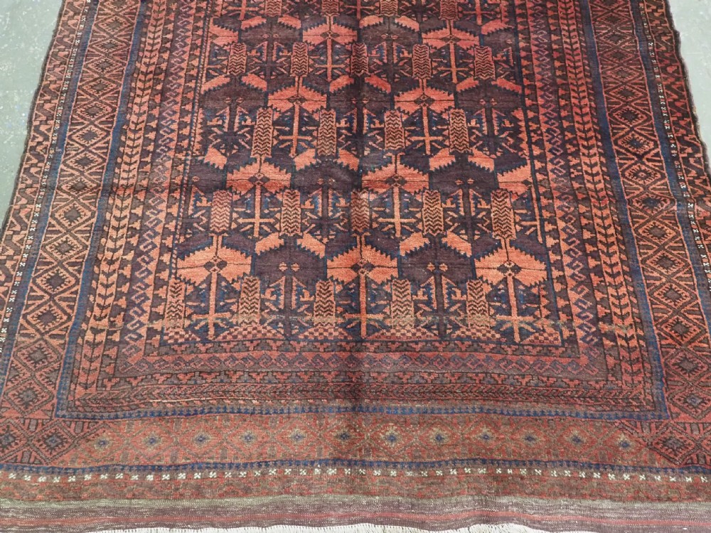 An antique Afghan Baluch hand-knotted wool rug featuring dark red, indigo, and terracotta geometric repeating motifs and ornate multi-layered borders. View V