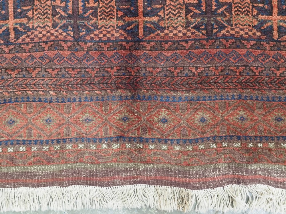 An antique Afghan Baluch hand-knotted wool rug featuring dark red, indigo, and terracotta geometric repeating motifs and ornate multi-layered borders. View VI