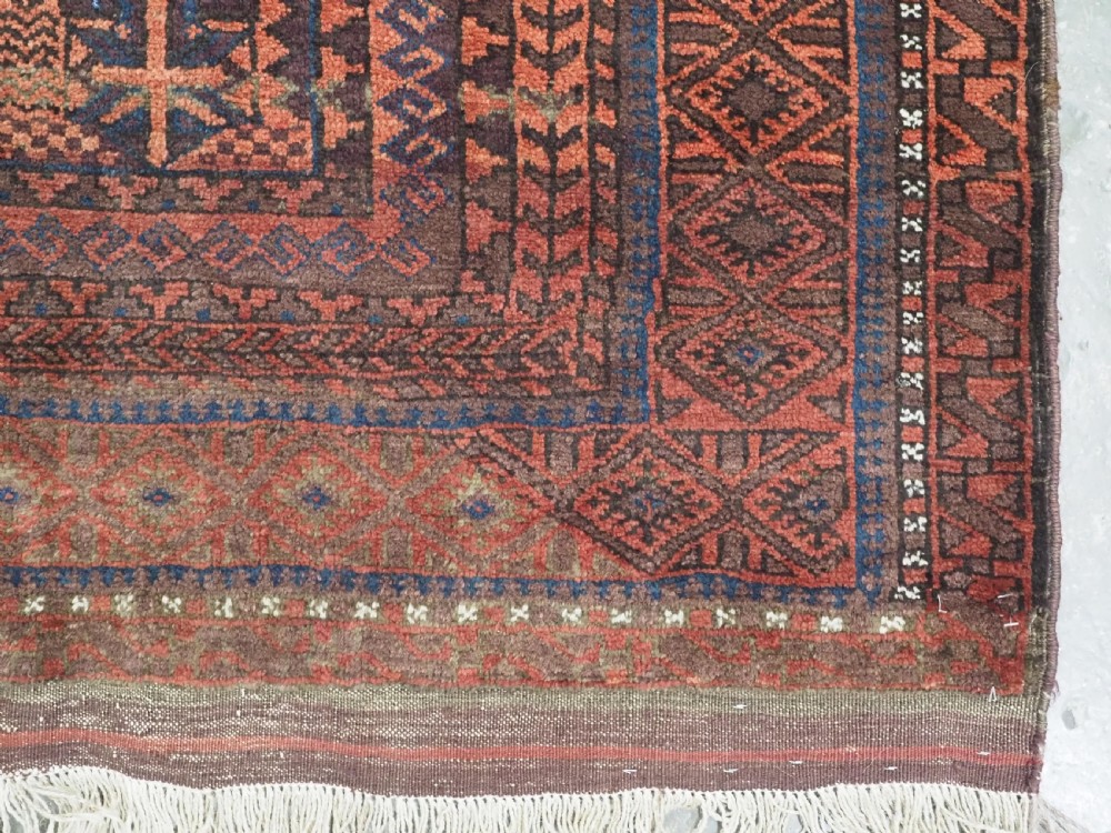 An antique Afghan Baluch hand-knotted wool rug featuring dark red, indigo, and terracotta geometric repeating motifs and ornate multi-layered borders. View VII