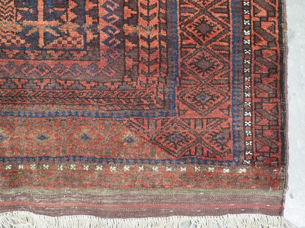 An antique Afghan Baluch hand-knotted wool rug featuring dark red, indigo, and terracotta geometric repeating motifs and ornate multi-layered borders. View VIII