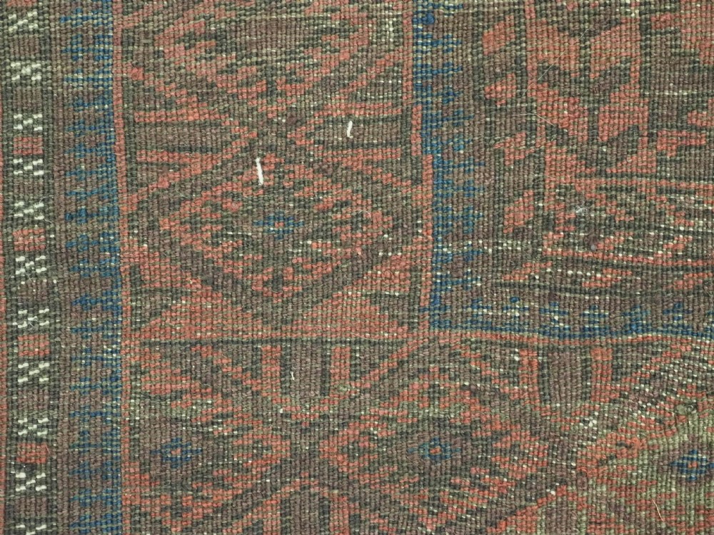 An antique Afghan Baluch hand-knotted wool rug featuring dark red, indigo, and terracotta geometric repeating motifs and ornate multi-layered borders. View IX