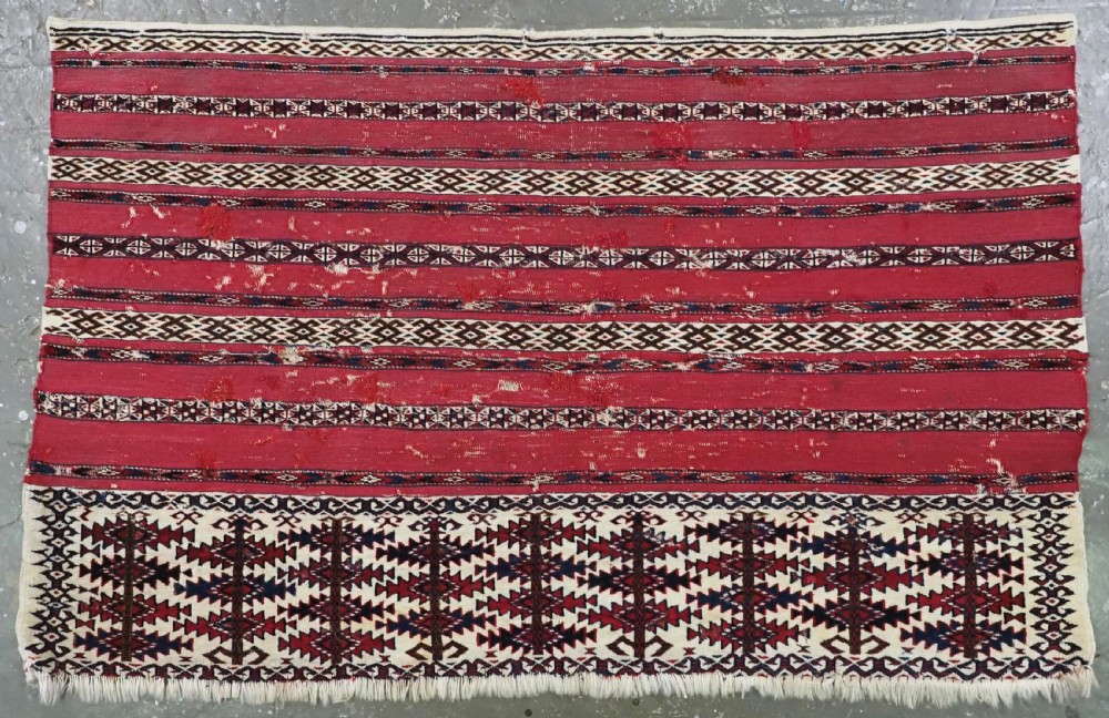 An antique Tekke Turkmen Ak chuval face displaying red and dark blue horizontal bands above a patterned ivory geometric lower panel.