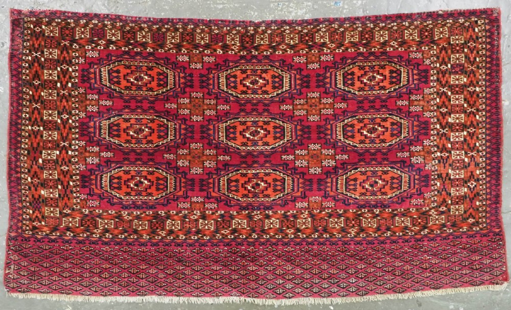 An antique woven wool Turkmen chuval face featuring nine primary octagonal gul motifs on a deep red field framed by geometric borders.