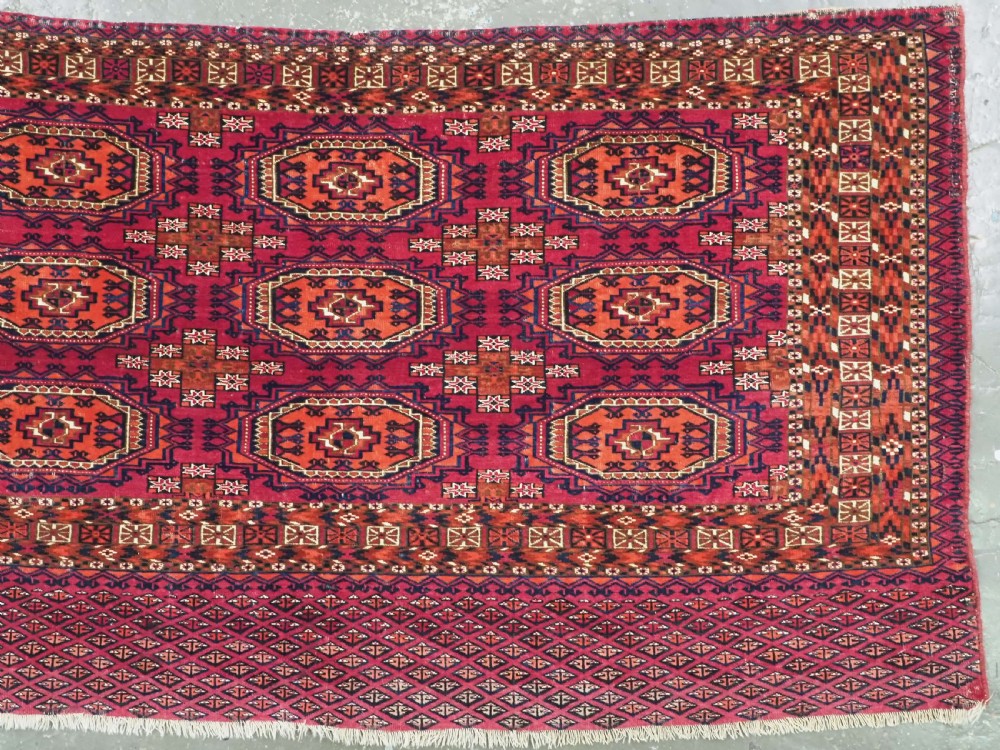 An antique woven wool Turkmen chuval face featuring nine primary octagonal gul motifs on a deep red field framed by geometric borders. View III