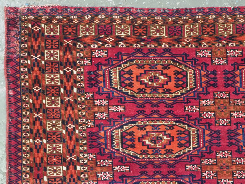 An antique woven wool Turkmen chuval face featuring nine primary octagonal gul motifs on a deep red field framed by geometric borders. View IV