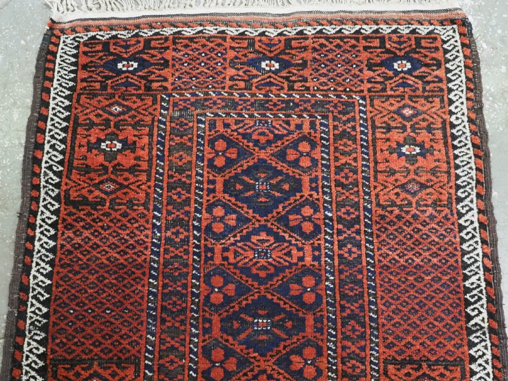 An antique rectangular Khorasan Baluch hand-knotted wool rug featuring repeating central dark blue geometric diamond motifs framed by multiple terracotta red pattern borders. View III
