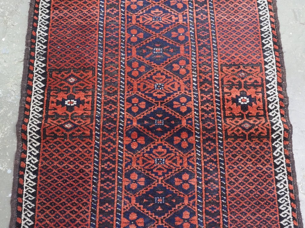 An antique rectangular Khorasan Baluch hand-knotted wool rug featuring repeating central dark blue geometric diamond motifs framed by multiple terracotta red pattern borders. View IV