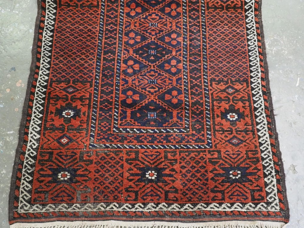 An antique rectangular Khorasan Baluch hand-knotted wool rug featuring repeating central dark blue geometric diamond motifs framed by multiple terracotta red pattern borders. View V