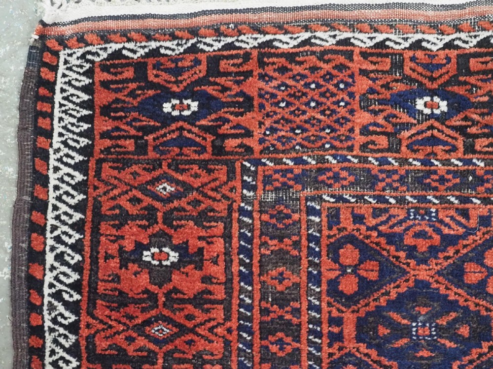 An antique rectangular Khorasan Baluch hand-knotted wool rug featuring repeating central dark blue geometric diamond motifs framed by multiple terracotta red pattern borders. View VI