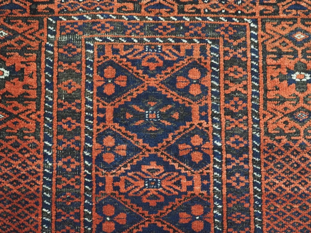 An antique rectangular Khorasan Baluch hand-knotted wool rug featuring repeating central dark blue geometric diamond motifs framed by multiple terracotta red pattern borders. View VIII