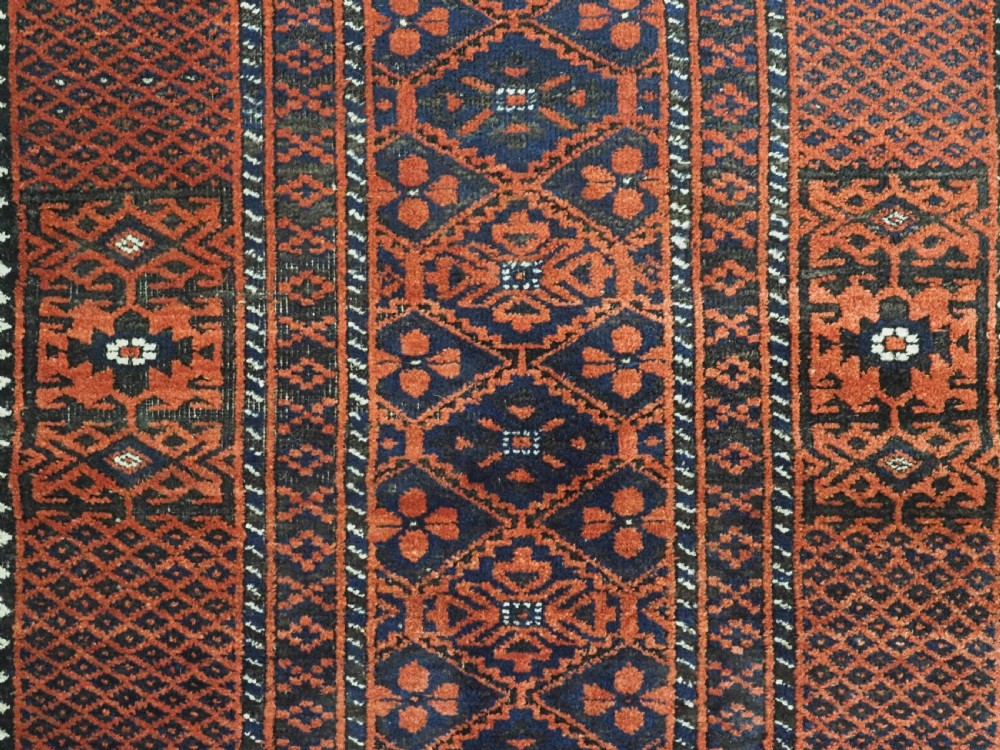 An antique rectangular Khorasan Baluch hand-knotted wool rug featuring repeating central dark blue geometric diamond motifs framed by multiple terracotta red pattern borders. View IX