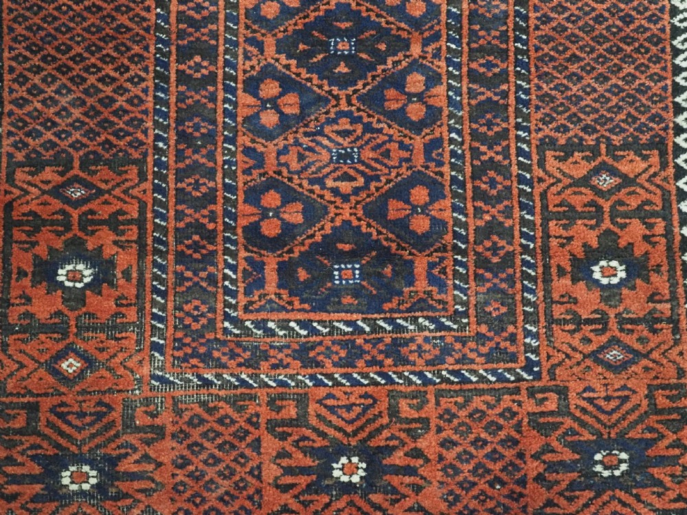 An antique rectangular Khorasan Baluch hand-knotted wool rug featuring repeating central dark blue geometric diamond motifs framed by multiple terracotta red pattern borders. View X