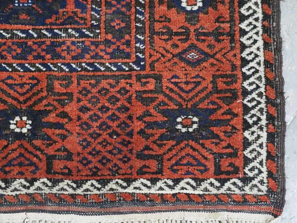 An antique rectangular Khorasan Baluch hand-knotted wool rug featuring repeating central dark blue geometric diamond motifs framed by multiple terracotta red pattern borders. View XI