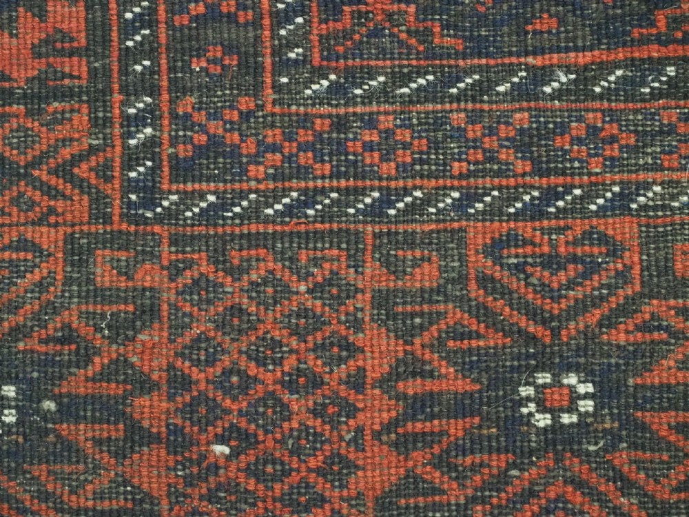 An antique rectangular Khorasan Baluch hand-knotted wool rug featuring repeating central dark blue geometric diamond motifs framed by multiple terracotta red pattern borders. View XII