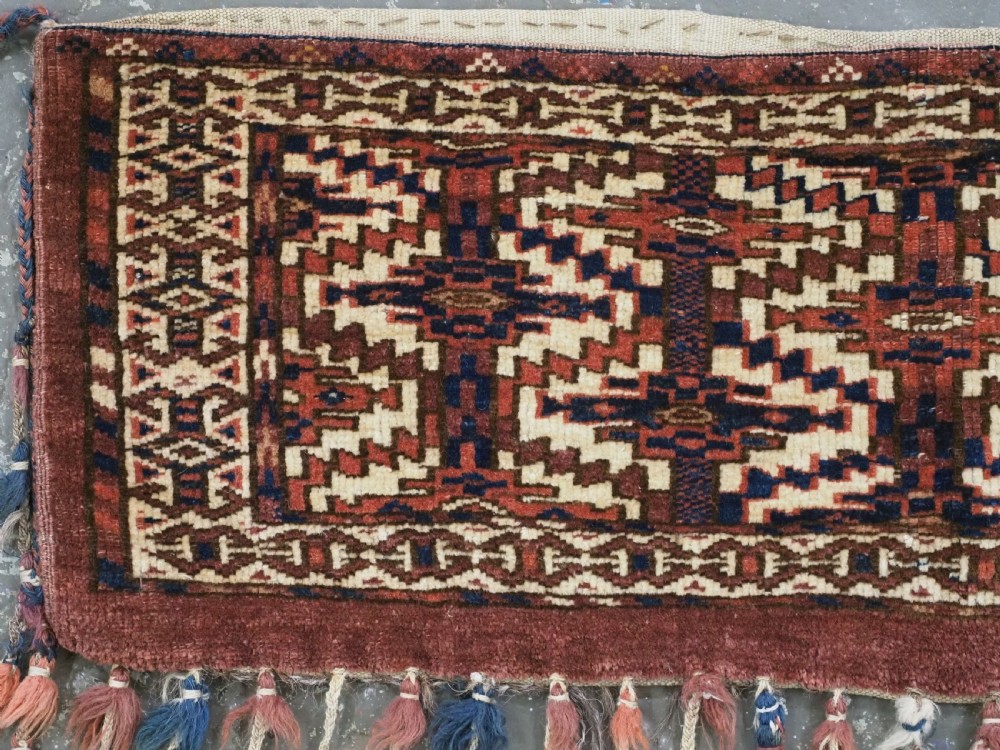 An antique rectangular Yomut Turkmen wool textile featuring intricate geometric lattice patterns in terracotta red, navy blue, and ivory, finished with a fringe of multi-coloured tassels along the bottom edge. View II