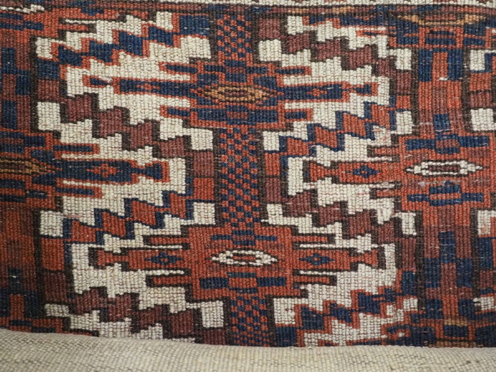 An antique rectangular Yomut Turkmen wool textile featuring intricate geometric lattice patterns in terracotta red, navy blue, and ivory, finished with a fringe of multi-coloured tassels along the bottom edge. View VIII