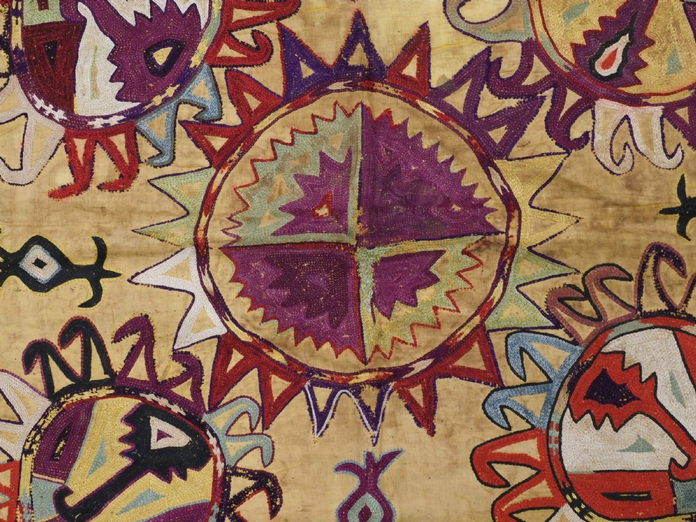 A square antique Uzbek Lakai embroidered textile featuring central circular and solar motifs in purple, red, and turquoise on a yellow fabric ground, finished with a multi-coloured fringed border. View VI