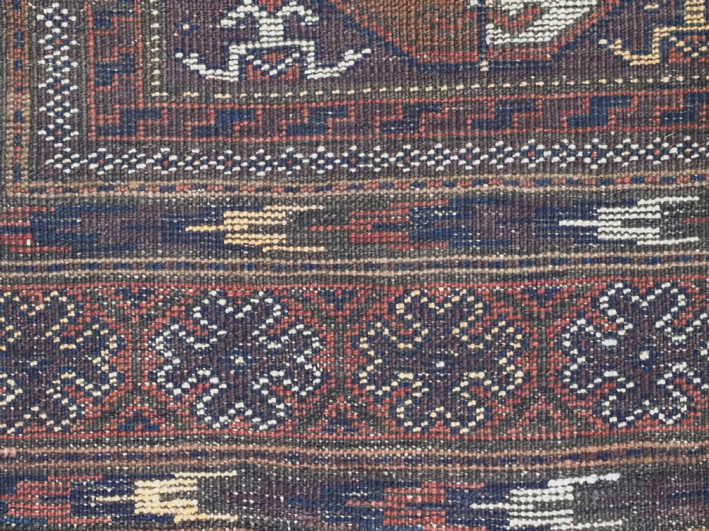 An antique woven wool Baluch rug featuring repeating octagonal Turkmen gul motifs in dark brown, terracotta, navy blue, and ivory with geometric borders. View XI