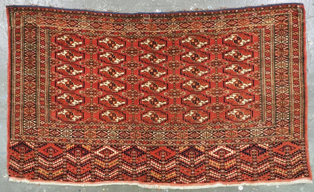 An antique Tekke Turkmen chuval bag face featuring repeating geometric gul motifs on a rust red wool pile with a detailed elem skirt border.