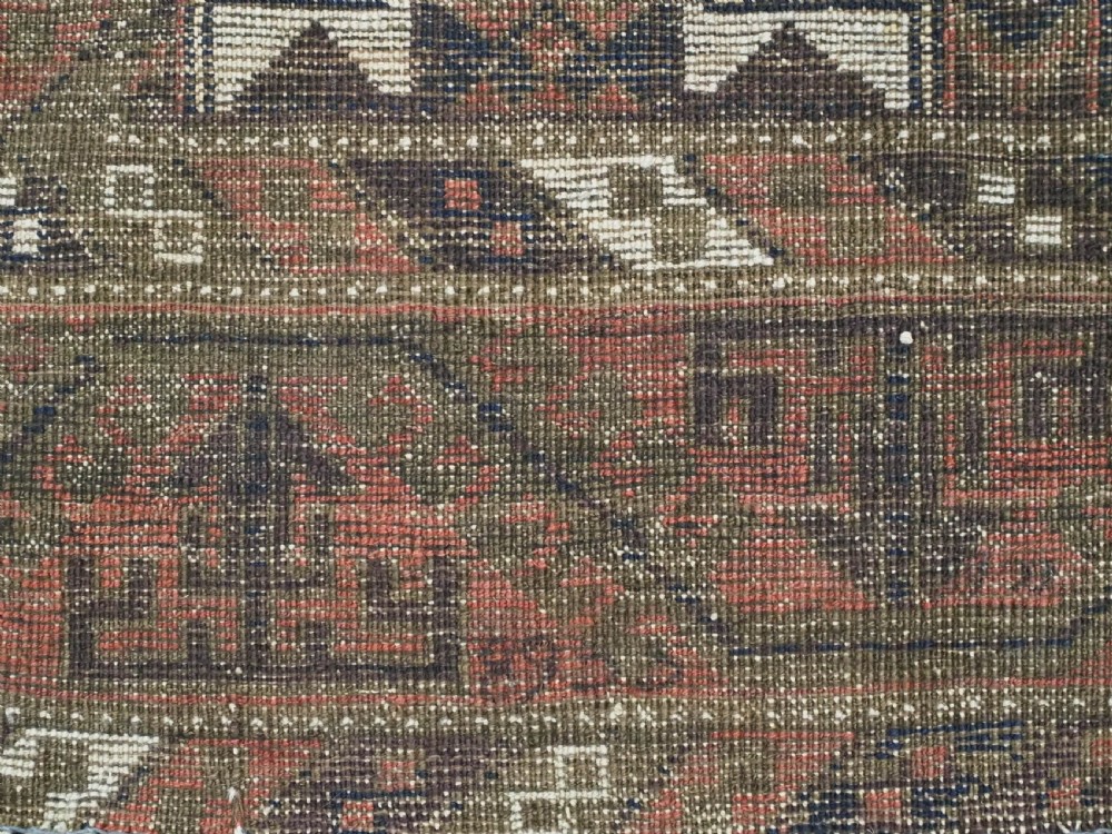 An antique hand-knotted Baluch wool rug displaying repeating geometric cruciform and octagonal motifs in terracotta red, navy blue, and dark brown tones. View XI