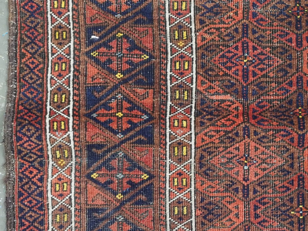 An antique rectangular Baluch wool rug featuring a terracotta geometric lattice pattern on a dark field surrounded by framed patterned borders. View VII