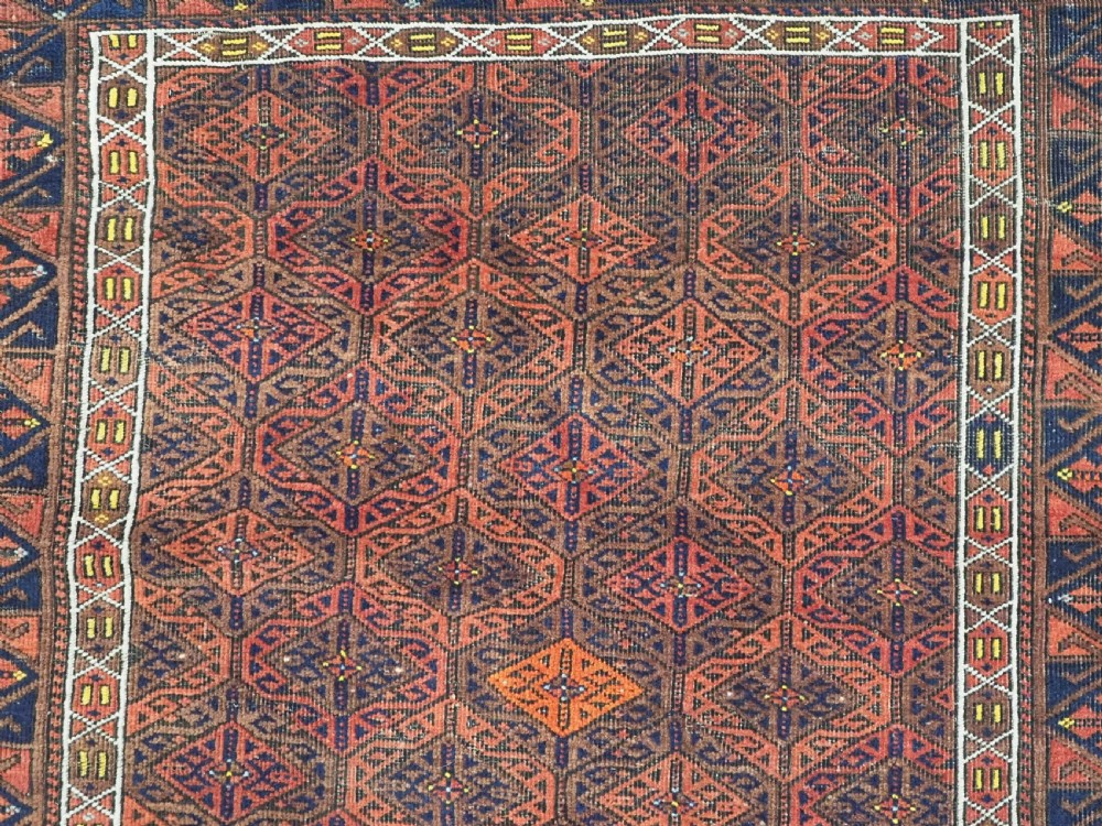 An antique rectangular Baluch wool rug featuring a terracotta geometric lattice pattern on a dark field surrounded by framed patterned borders. View VIII