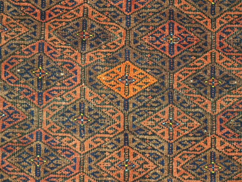 An antique rectangular Baluch wool rug featuring a terracotta geometric lattice pattern on a dark field surrounded by framed patterned borders. View IX