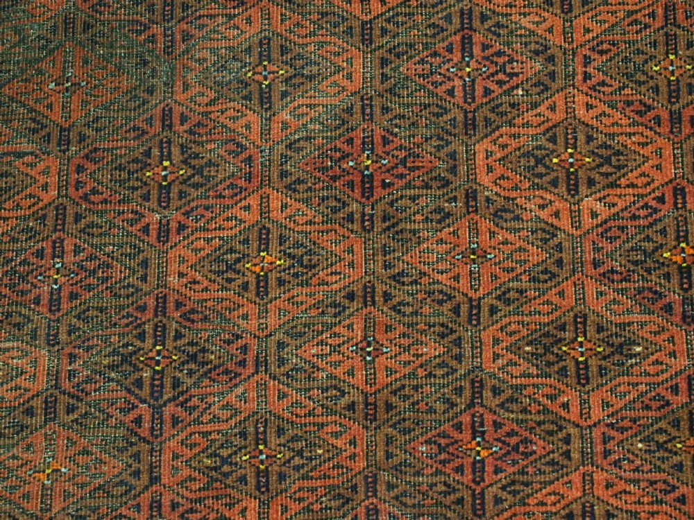 An antique rectangular Baluch wool rug featuring a terracotta geometric lattice pattern on a dark field surrounded by framed patterned borders. View X