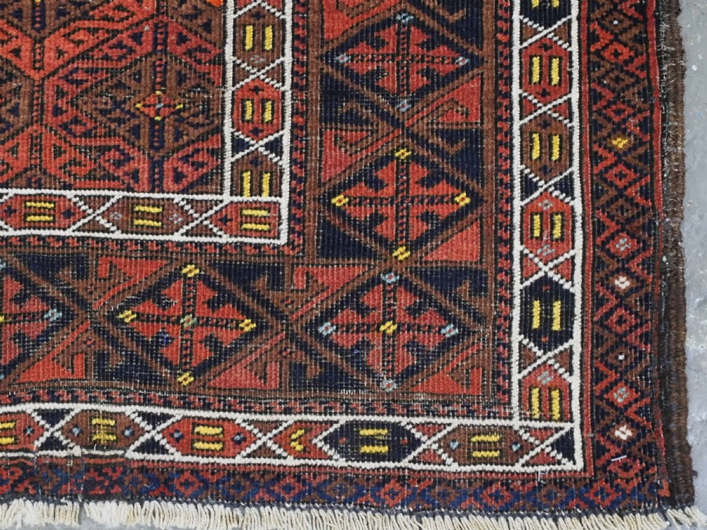 An antique rectangular Baluch wool rug featuring a terracotta geometric lattice pattern on a dark field surrounded by framed patterned borders. View XI