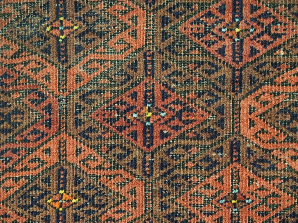 An antique rectangular Baluch wool rug featuring a terracotta geometric lattice pattern on a dark field surrounded by framed patterned borders. View XIII
