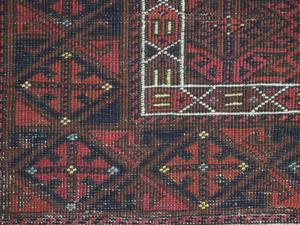 An antique rectangular Baluch wool rug featuring a terracotta geometric lattice pattern on a dark field surrounded by framed patterned borders. View XIV