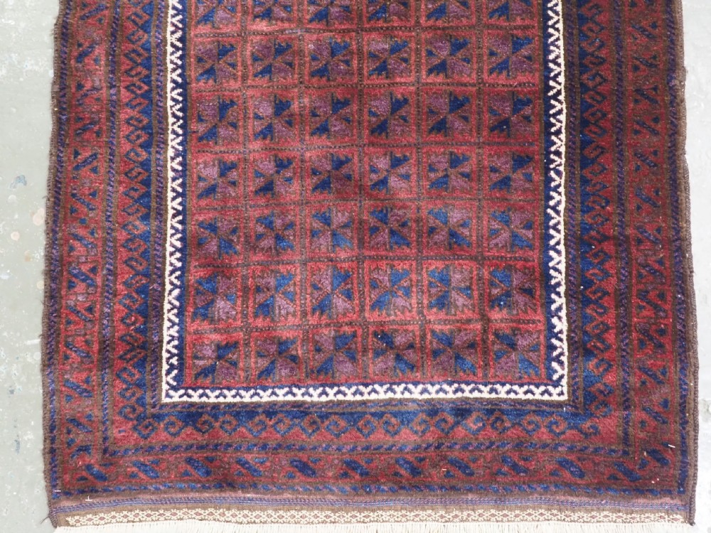 An antique hand-knotted Baluch wool prayer rug featuring a central mihrab arch motif with repeat geometric lotus leaf patterns in deep red, navy blue, and white. View IV