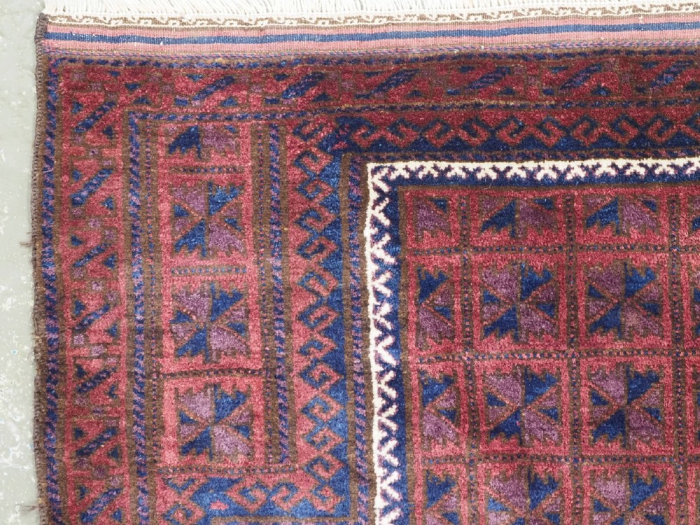 An antique hand-knotted Baluch wool prayer rug featuring a central mihrab arch motif with repeat geometric lotus leaf patterns in deep red, navy blue, and white. View V