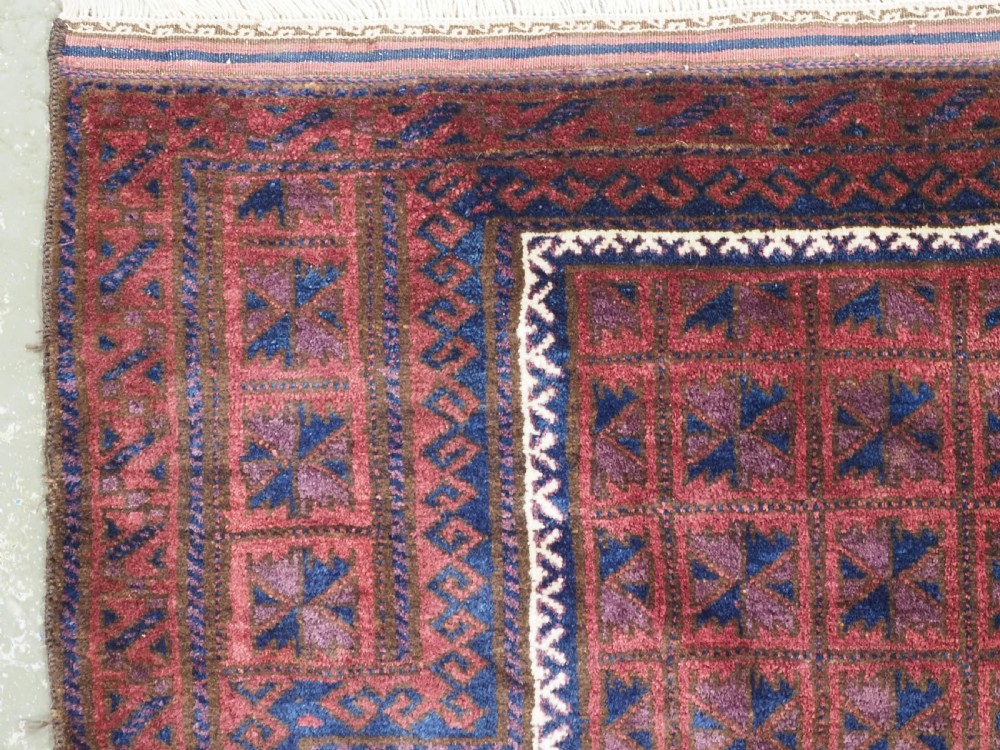 An antique hand-knotted Baluch wool prayer rug featuring a central mihrab arch motif with repeat geometric lotus leaf patterns in deep red, navy blue, and white. View VI