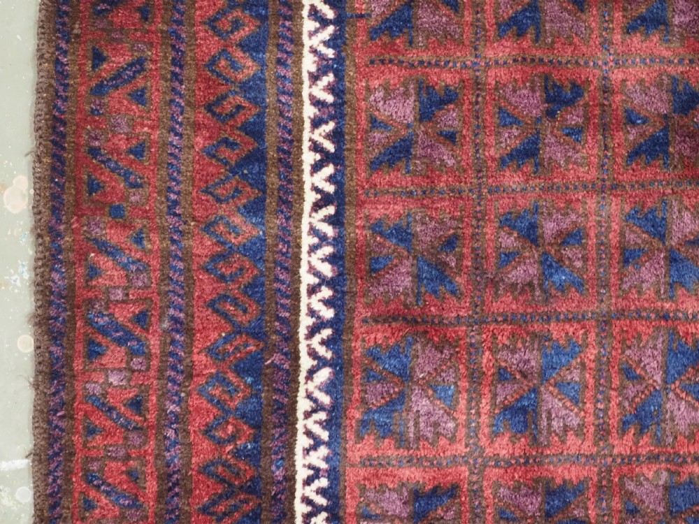 An antique hand-knotted Baluch wool prayer rug featuring a central mihrab arch motif with repeat geometric lotus leaf patterns in deep red, navy blue, and white. View VII
