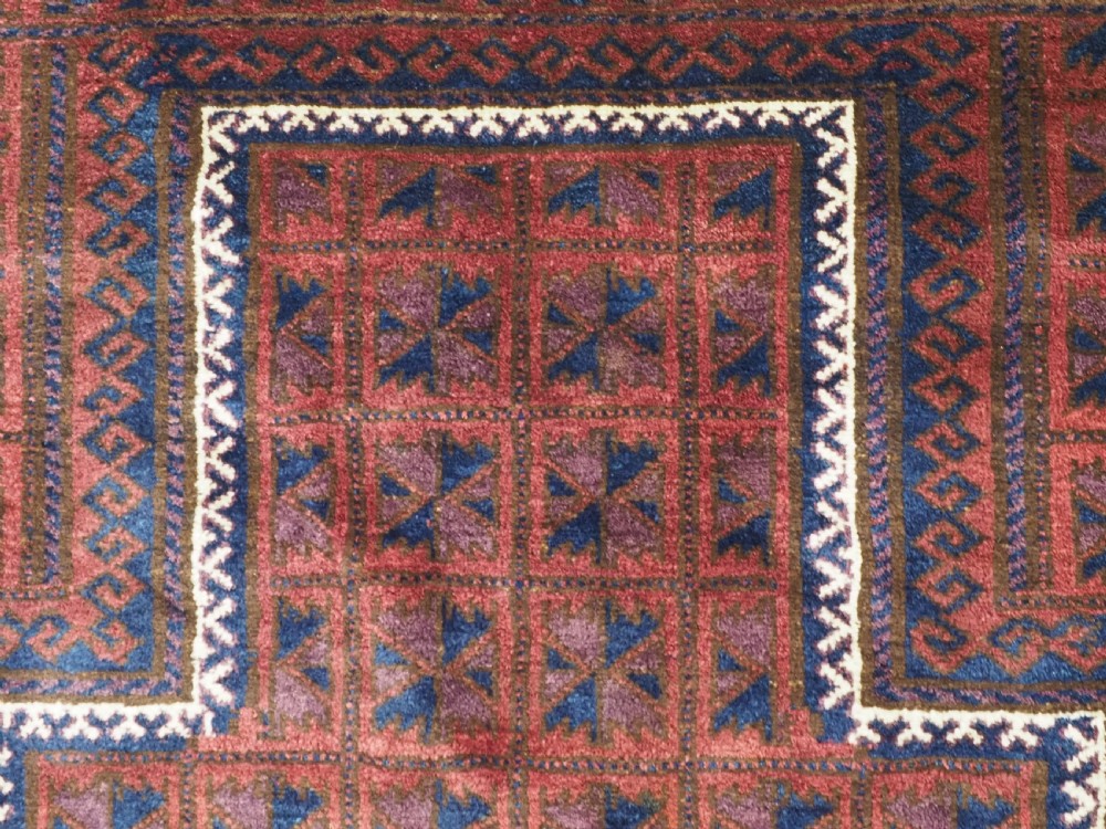 An antique hand-knotted Baluch wool prayer rug featuring a central mihrab arch motif with repeat geometric lotus leaf patterns in deep red, navy blue, and white. View VIII