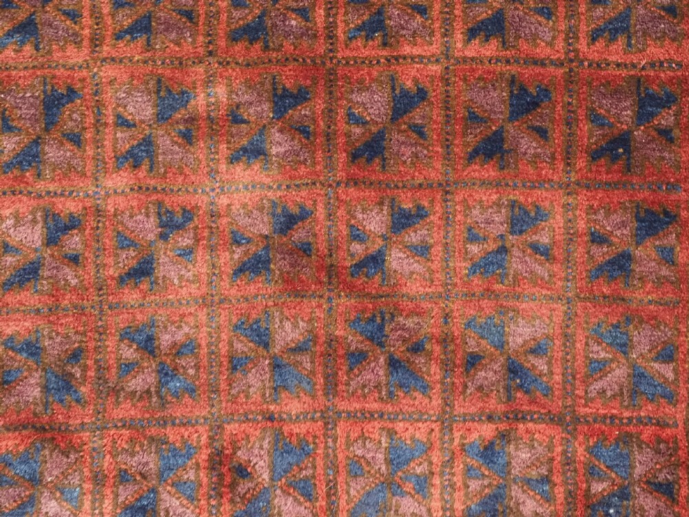 An antique hand-knotted Baluch wool prayer rug featuring a central mihrab arch motif with repeat geometric lotus leaf patterns in deep red, navy blue, and white. View IX