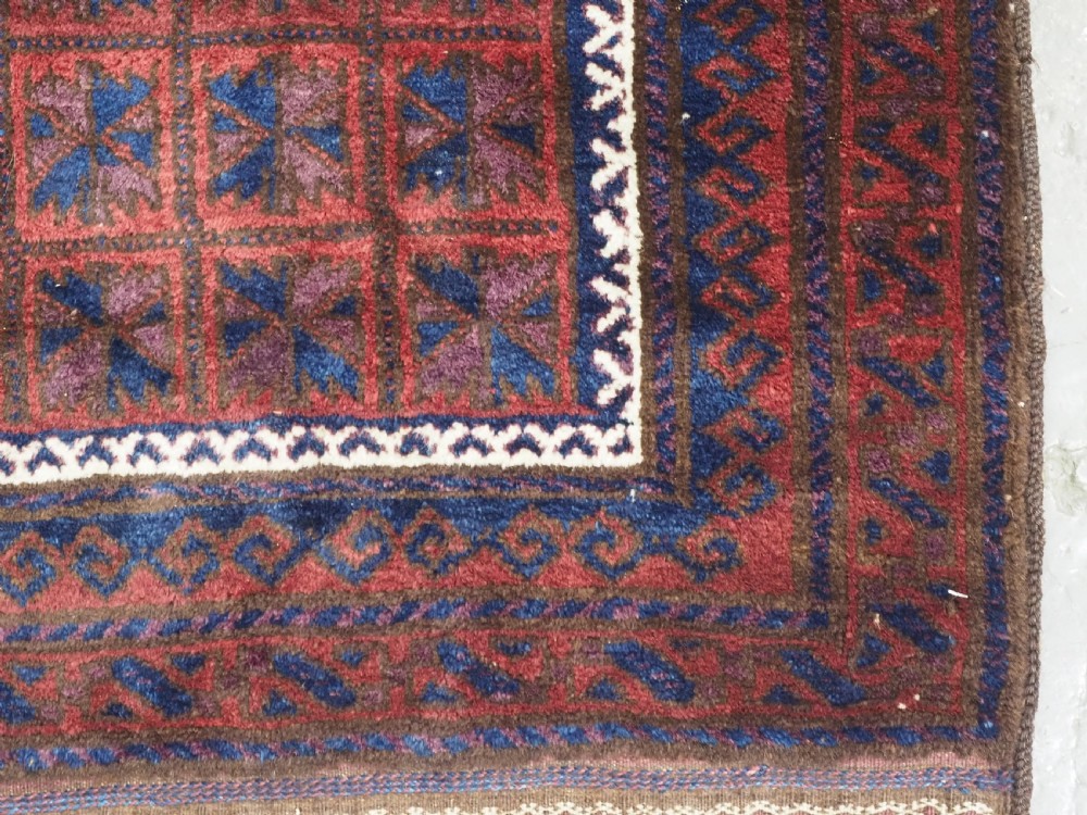An antique hand-knotted Baluch wool prayer rug featuring a central mihrab arch motif with repeat geometric lotus leaf patterns in deep red, navy blue, and white. View X