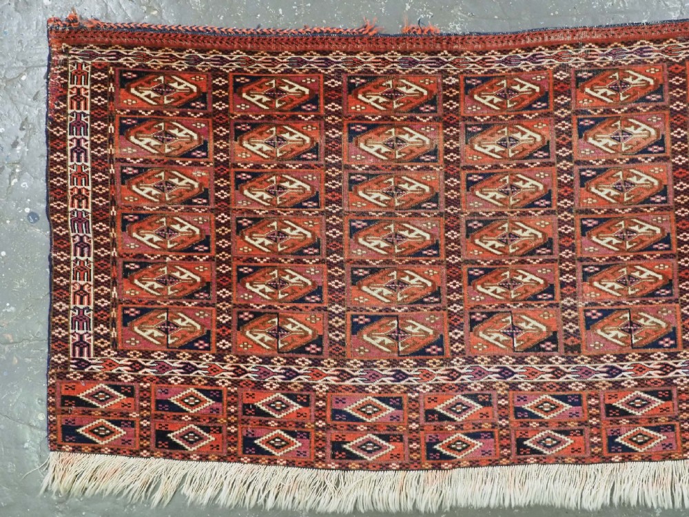 A hand-knotted wool Tekke Turkmen chuval face with repeating geometric aina gul motifs in red, navy blue, and ivory tones, finished with a fringed lower border. View II
