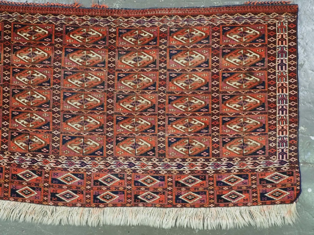 A hand-knotted wool Tekke Turkmen chuval face with repeating geometric aina gul motifs in red, navy blue, and ivory tones, finished with a fringed lower border. View III