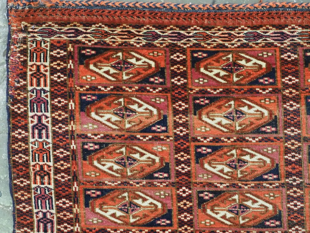 A hand-knotted wool Tekke Turkmen chuval face with repeating geometric aina gul motifs in red, navy blue, and ivory tones, finished with a fringed lower border. View IV
