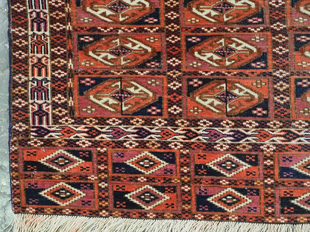 A hand-knotted wool Tekke Turkmen chuval face with repeating geometric aina gul motifs in red, navy blue, and ivory tones, finished with a fringed lower border. View V