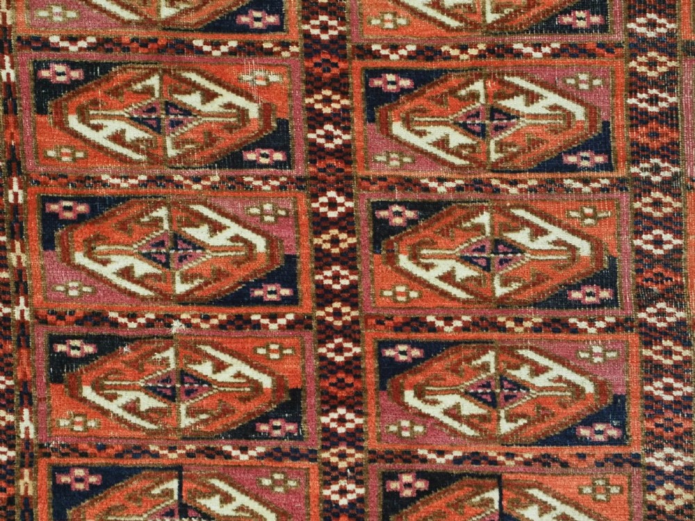 A hand-knotted wool Tekke Turkmen chuval face with repeating geometric aina gul motifs in red, navy blue, and ivory tones, finished with a fringed lower border. View VI