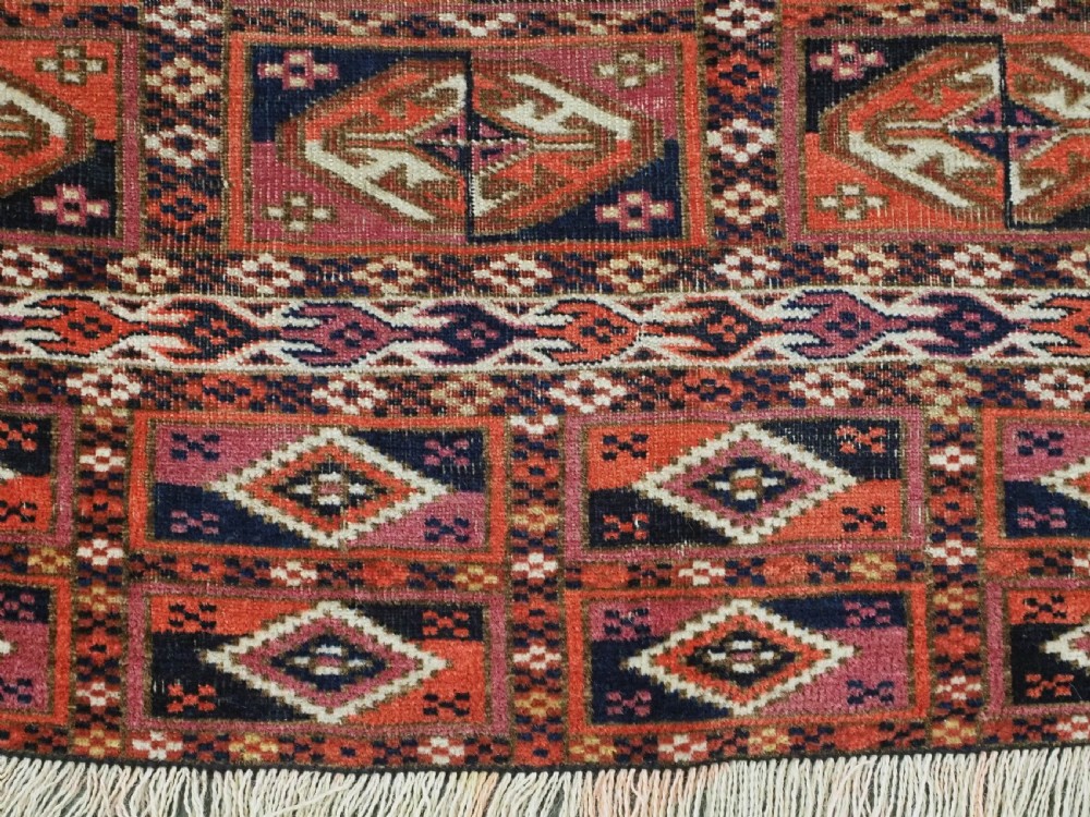 A hand-knotted wool Tekke Turkmen chuval face with repeating geometric aina gul motifs in red, navy blue, and ivory tones, finished with a fringed lower border. View VII
