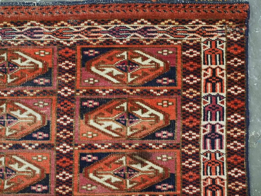 A hand-knotted wool Tekke Turkmen chuval face with repeating geometric aina gul motifs in red, navy blue, and ivory tones, finished with a fringed lower border. View IX